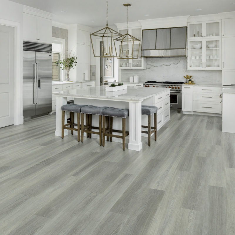 Beautiful kitchen interior in new luxury home, with white cabinets and woodwork, pendant lights, stainless steel appliances, and large kitchen island. Features stainless steel range hood.